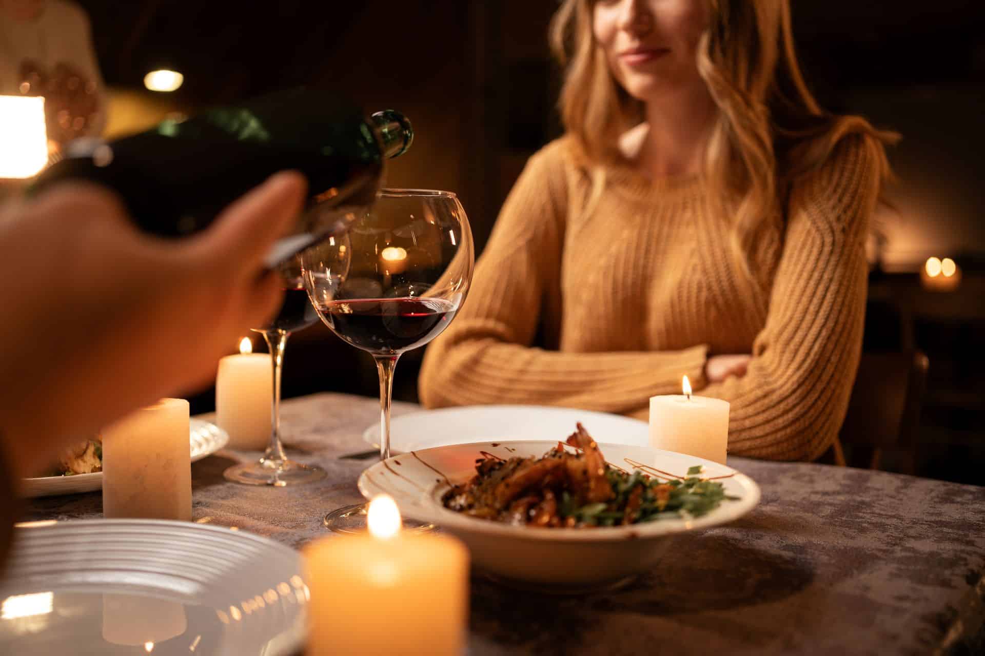 Frau sitzt bei Kerzenschein beim Abendessen mit Rotwein
