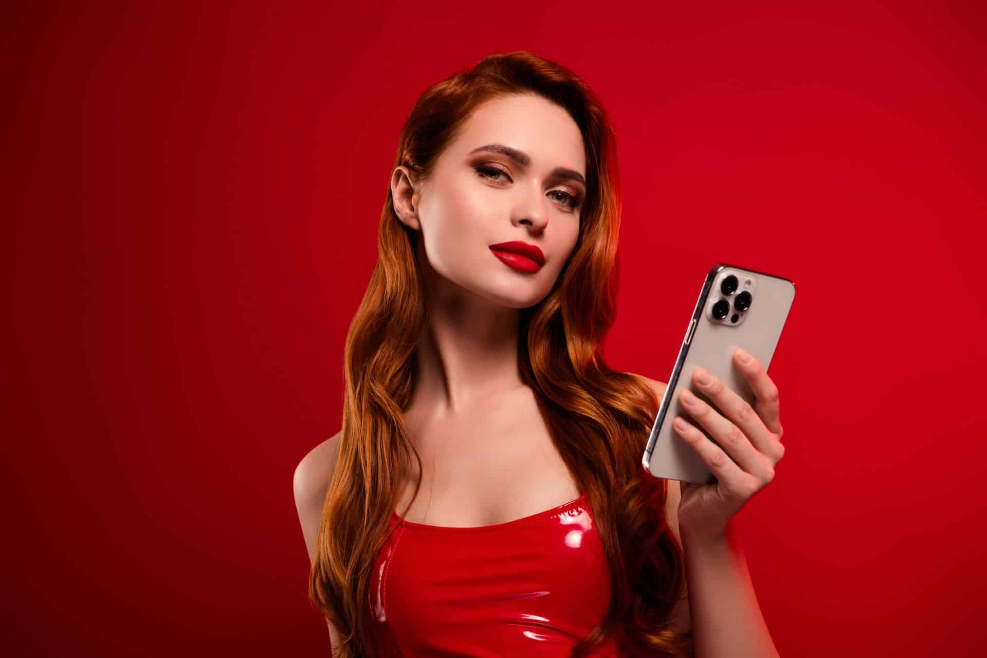 Rothaarige Frau in rotem Kleid mit Smartphone vor rotem Hintergrund